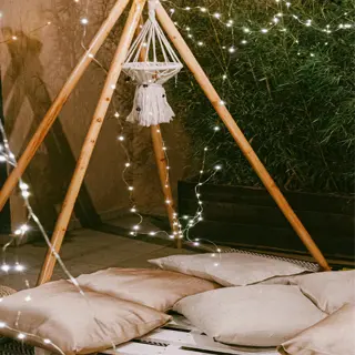 a bamboo teepee with soft cushions on a pallet, adorned with string lights, creating a cozy outdoor seating area