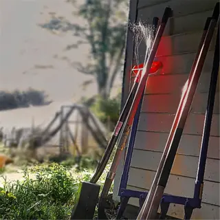 a broadfork leans against a wooden wall, with other garden tools nearby, illuminated by dramatic lighting