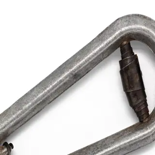 a close-up of a metal olive pitter with a rusty handle and a white background