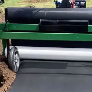 a green and black mulch layer tool laying down a roll of black mulch on the ground
