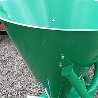 a green metal seed spreader on a gravel surface