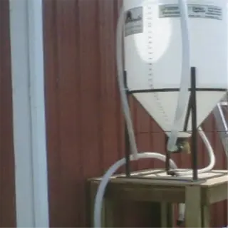 a large white container with hoses attached, mounted on a wooden stand against a red barn wall