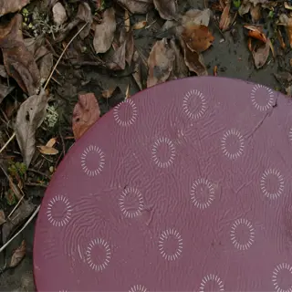 a maroon gardening kneeling pad with a circular pattern, placed on the ground among fallen leaves