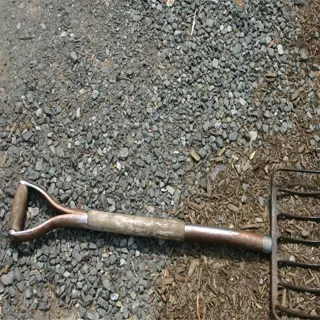 a metal mulching fork lies on the ground, surrounded by mulch and gravel