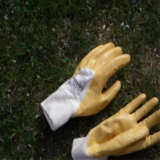 a pair of yellow gardening gloves with white cuffs, laid on a grassy surface