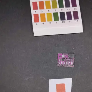a ph test strip with a color chart and a small electronic component