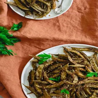a plate of spiced snap pea snacks garnished with parsley, served on an orange napkin with a side of red pepper flakes