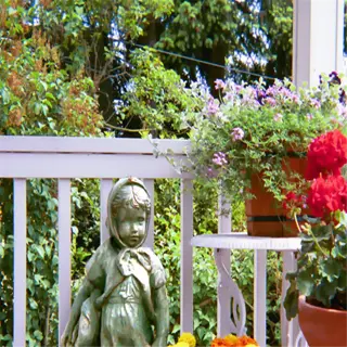 a porch with various potted plants, including geraniums and marigolds, and a small statue