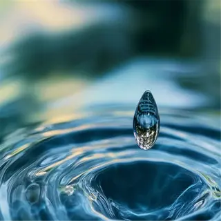 a precise water droplet creating ripples on a calm surface