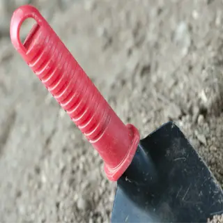 a red-handled garden trowel partially buried in soil