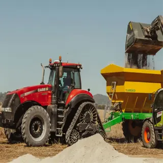 a tractor and loader filling a fertilizer spreader with material