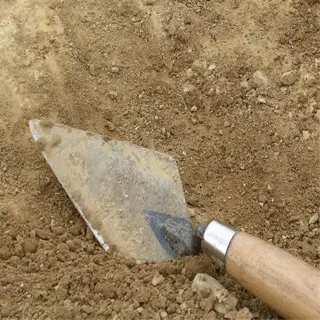 a trowel with a wooden handle resting on the soil