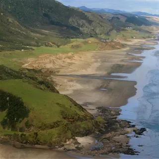 aerial view of a rugged coastal landscape with a sandy beach, rocky outcrops, and lush green hills