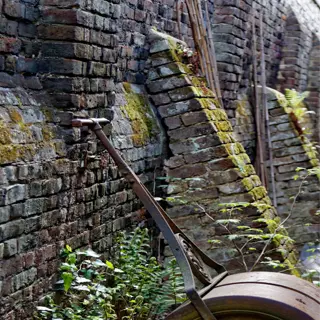 an old rusty lawn roller leans against a mossy brick wall