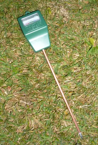 analog soil moisture meter with green display head and probe resting on a grassy surface