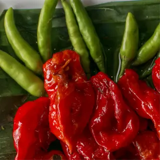 arrangement of ghost peppers with red and green chilies on banana leaf