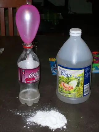 baking soda vinegar experiment: pink balloon on coca-cola bottle, great value vinegar jug, and baking soda pile - classic chemical reaction demo setup
