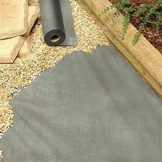 biodegradable garden fabric roll partially unrolled on gravel path with stone borders and plants