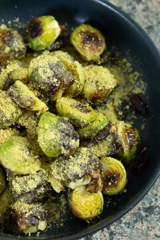 black bowl of grilled brussels sprouts with charred edges and yellow seasoning, served on a granite countertop