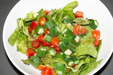 bowl of fresh okra salad with crisp lettuce, cherry tomatoes, and sliced green okra pods, dressed with vinaigrette