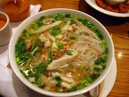 bowl of lemongrass pho soup with chicken, rice noodles, green onions, and cilantro on a wooden restaurant table