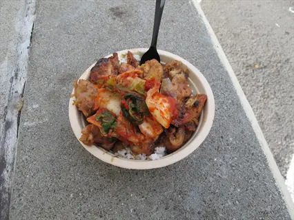 bowl of lemongrass rice bowl with grilled chicken, kimchi, and fresh herbs on concrete surface. black fork inserted