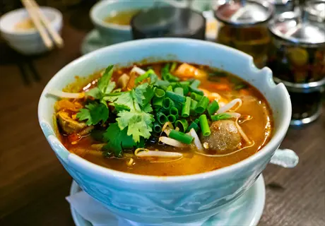 bowl of tom yum soup with mushrooms, bean sprouts, and cilantro garnish, served in a restaurant setting