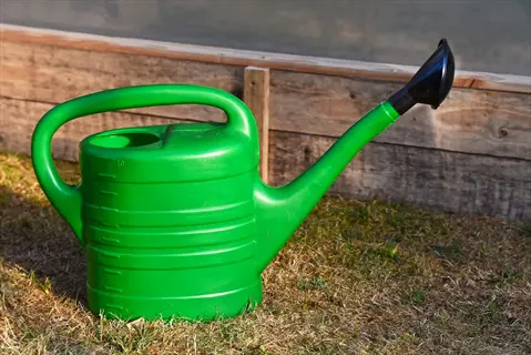 bright green plastic watering can container with measurement markings on a grassy surface near wooden garden edging