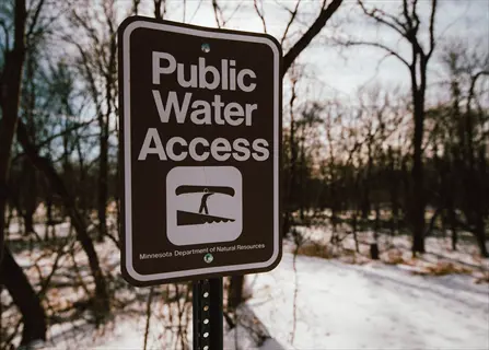 brown 'public water access' sign with canoe symbol in snowy forest landscape, issued by minnesota department of natural resources