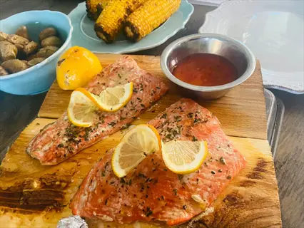 cedar-planked dill salmon marinade with lemon slices, served with roasted potatoes and corn on the cob