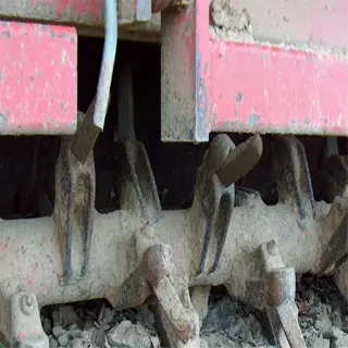 close-up of a rototiller's digging tines, showing the attachment to the machine and the tilled soil