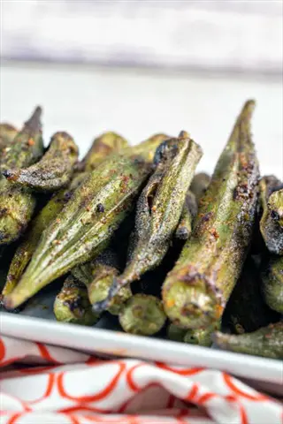 close-up of charred grilled okra pods with visible seasoning and grill marks, arranged on a white plate over an orange patterned cloth