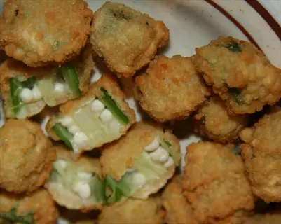 close-up of crispy fried okra pieces with golden-brown coating, some cut open revealing green interior and seeds, arranged on a plate
