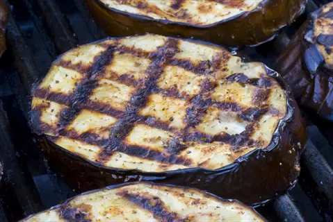 close-up of grilled eggplant slices with char marks cooking on a barbecue grill