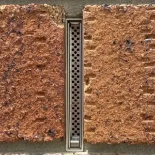 close-up of masonry weep hole with metal grate in brick wall. this stone raised bed weep hole is part of masonry drainage systems for garden structure drainage