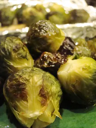close-up of roasted brussels sprouts with crispy, caramelized edges on a green plate, background shows foil-wrapped baking tray