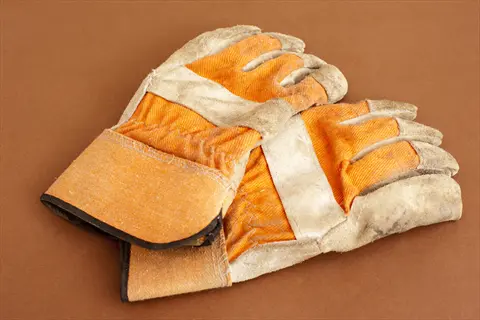 close-up of worn gardening gloves with orange fabric and light-colored cuffs on a brown background