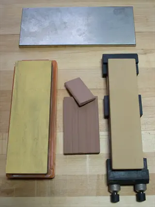collection of sharpening stones and a metal plate on a wooden work surface; sharpening stone garden tools are essential for maintaining pruning shears and loppers