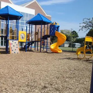 colorful playground equipment with blue roofs and yellow slides installed on wood fiber mulch surfacing. the natural wood chips cover the ground, providing impact-absorbing safety in this outdoor recreational area near a brick building