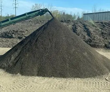 conical pile of aged manure soil being deposited by conveyor belt in outdoor industrial setting