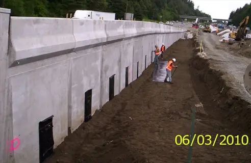 construction site showing concrete retaining wall installation with workers and geotextile fabric drainage, dated 06/03/2010