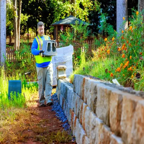 construction worker carrying concrete block near stone retaining wall to prevent soil erosion landscape