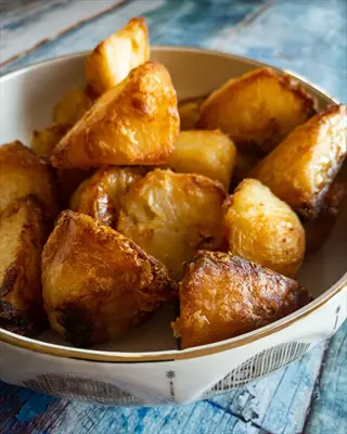 crispy roasted potatoes from cold climate regions: golden-brown chunks with fluffy interiors in a decorative bowl on weathered blue wood