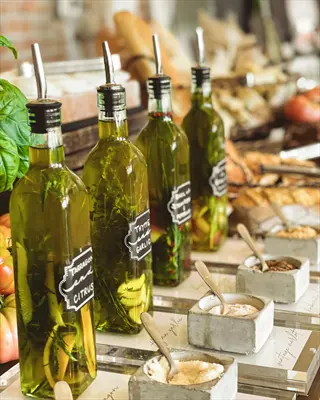 display of tarragon infused oil (tarragon and citrus bottle), other herb-infused oils, and salts with bread and basil in background