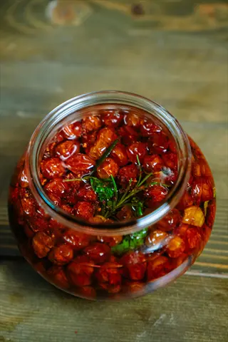 dried tomatoes jar with sun-dried tomatoes (amish paste variety) in oil and herbs on a rustic wooden table