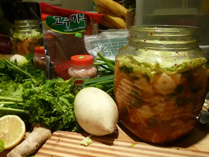 fermentation setup featuring jar water radish in brine, fresh radish, greens, and ingredient packages (including gochugaru and rice flour) for pickling