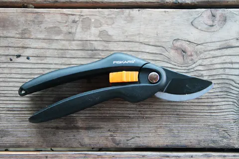 fiskars bypass hand pruners gardening tool on a weathered wooden surface, featuring ergonomic grips and sharp blade for pruning