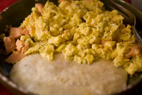 fluffy scrambled eggs dill with smoked salmon bits and creamy polenta, served in a dark bowl