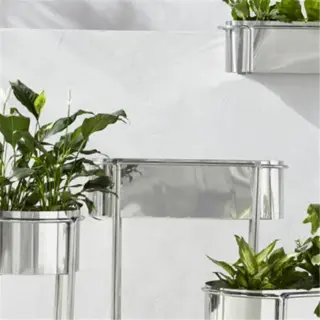 four stainless steel planters with green plants against a wall