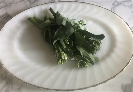 fresh gai lan (chinese broccoli) with leaves, stems, and flowers on a white decorative plate